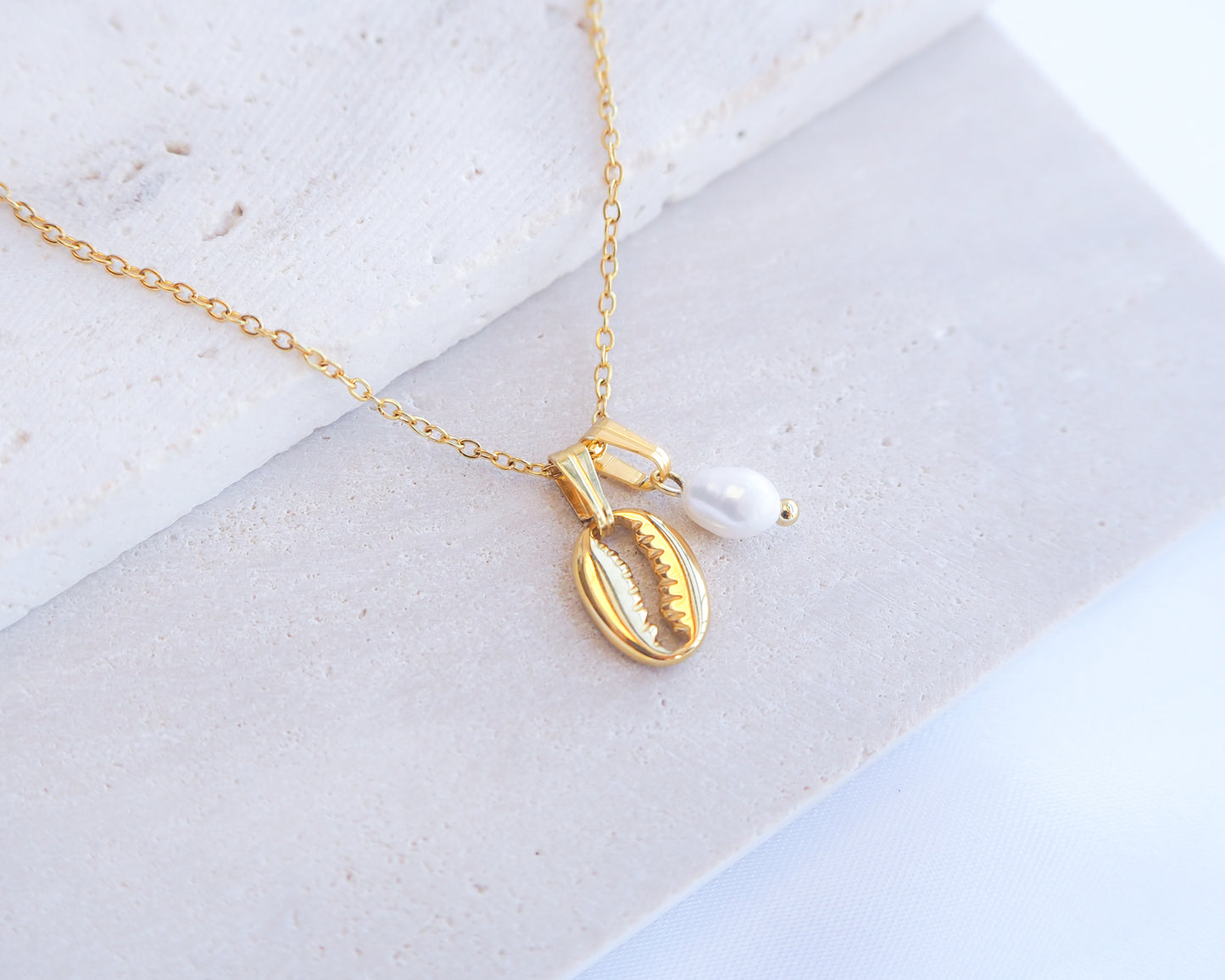 Gold necklace with a shell and pearl pendant on a light background. Gold Cowrie Shell Necklace with Pearl on display