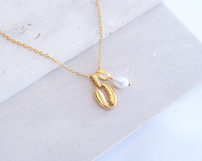 Gold necklace with a shell and pearl pendant on a light background. Gold Cowrie Shell Necklace with Pearl on display