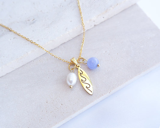 Gold Surfboard Necklace with Freshwater Pearl Angelite Beads on display. Gold surfboard pendant with freshwater pearl and gemstone beads. Made with premium 18k gold stainless steel. The gemstones is blue angelite. 
