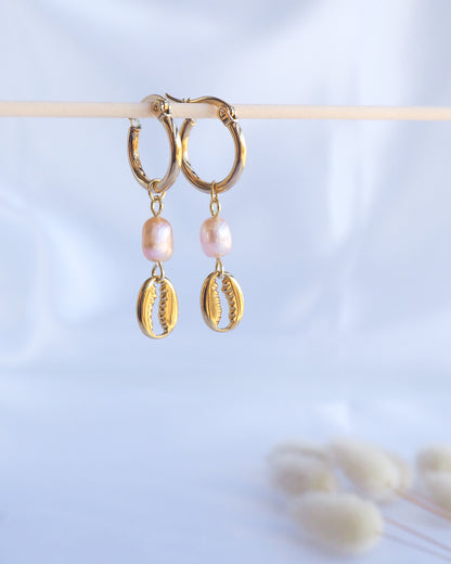 Gold hoop earrings with pink pearl and cowrie shell charms on a light blue background. Made with premium 14k and 18k gold stainless steel and pink freshwater pearl beads. 