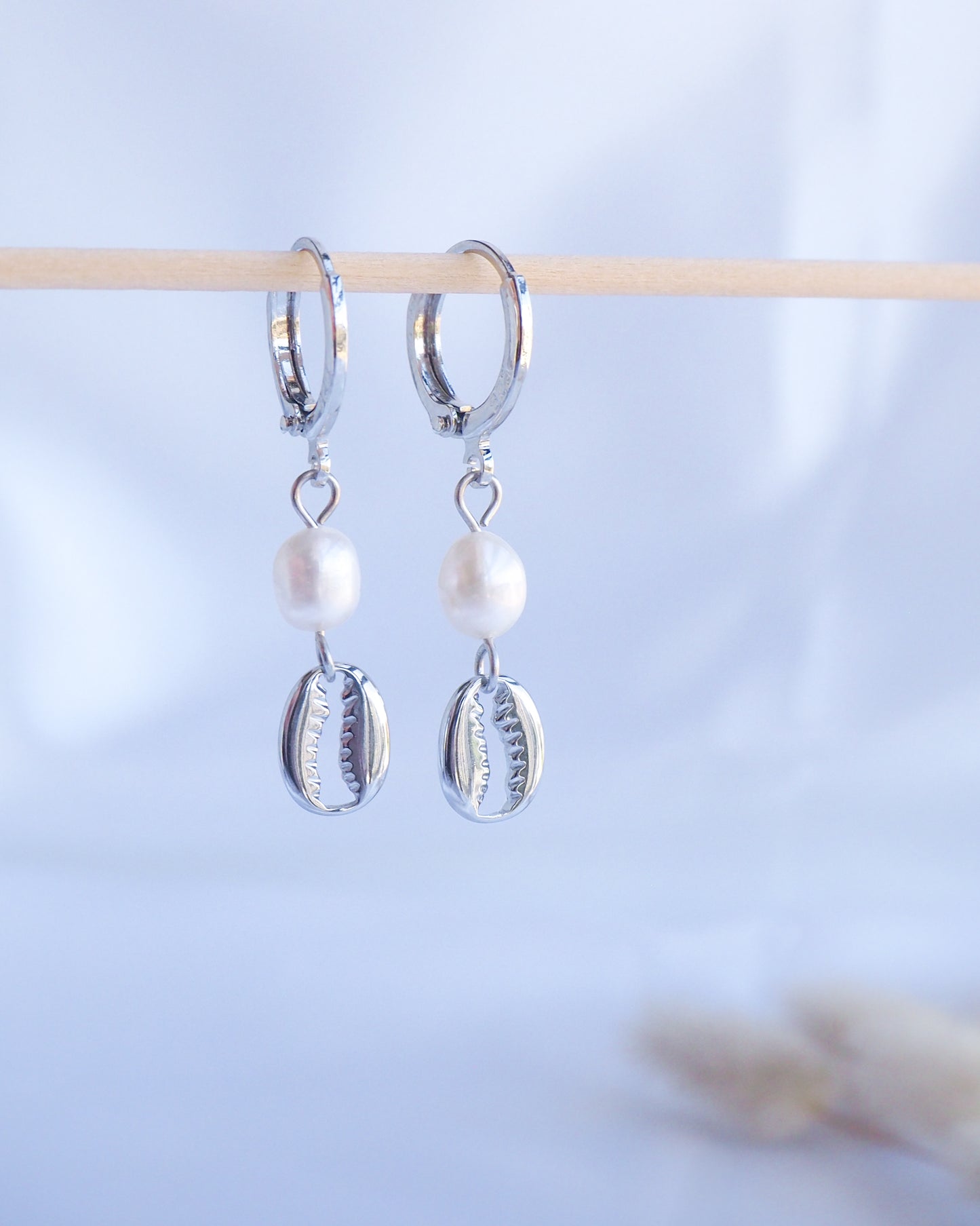 Silver hoop earrings with pearl and shell charms on a light blue background. Made with 925 sterling silver and white freshwater pearl beads. 