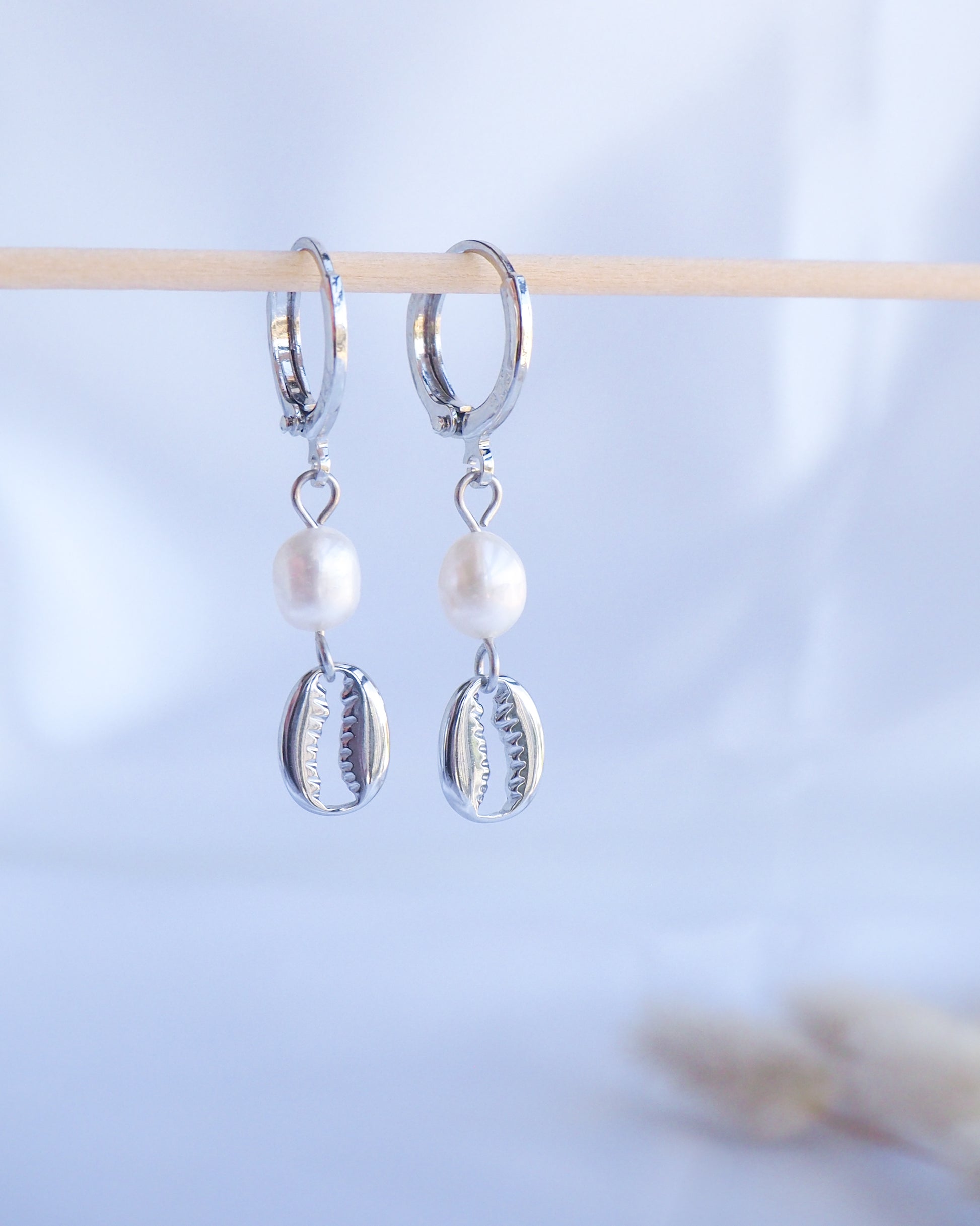 Silver hoop earrings with pearl and shell charms on a light blue background. Made with 925 sterling silver and white freshwater pearl beads. 
