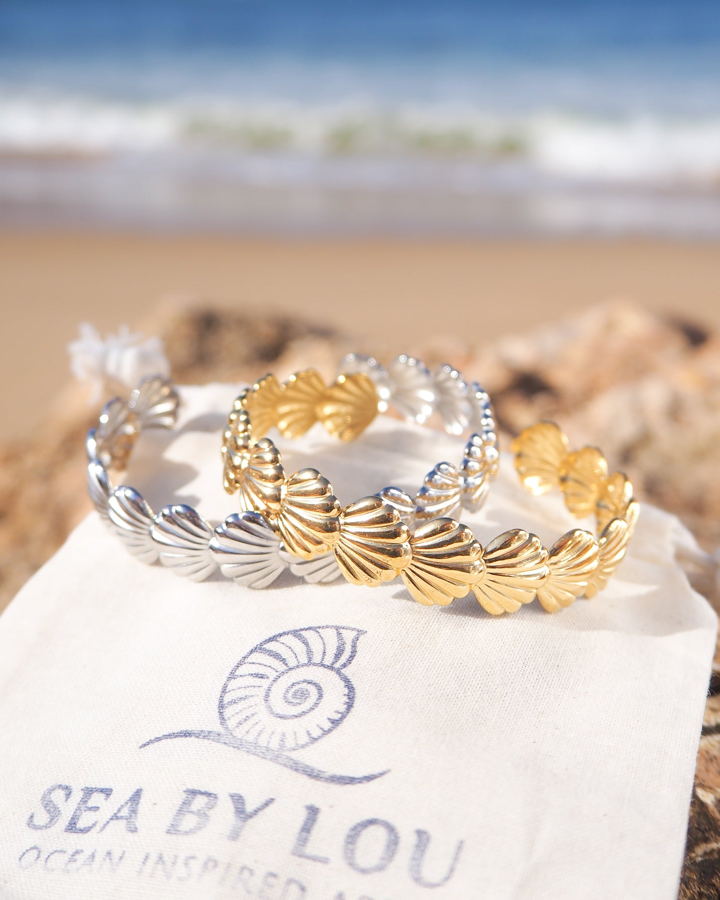 Two shell bracelets with horizontal scallop shells in 18k gold stainless steel and silver stainless steel with ocean background