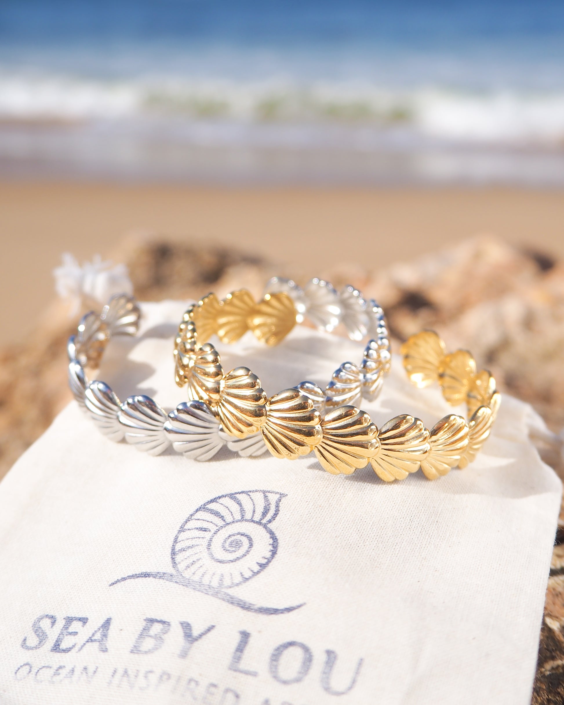 Two shell bracelets with horizontal scallop shells in 18k gold stainless steel and silver stainless steel with ocean background