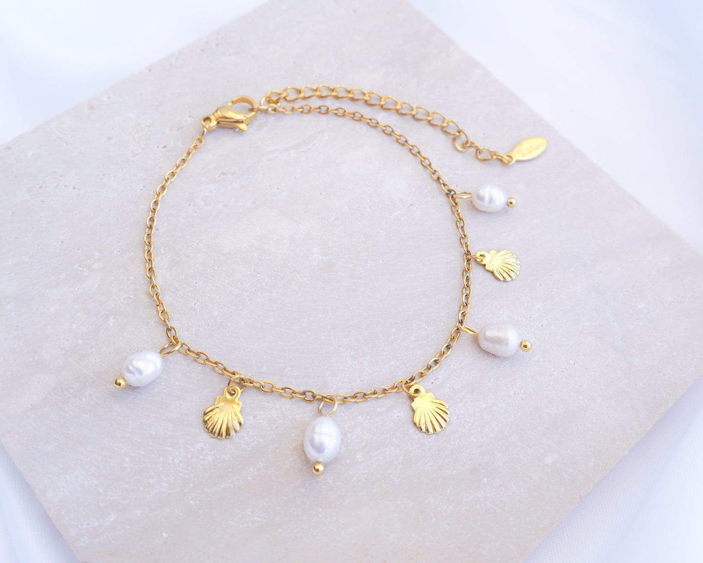 Gold bracelet with shell and pearl charms on a white background. Gold Tiny Shell White Freshwater Pearl Bracelet displayed on stone, Dainty Gold Shell Bracelet