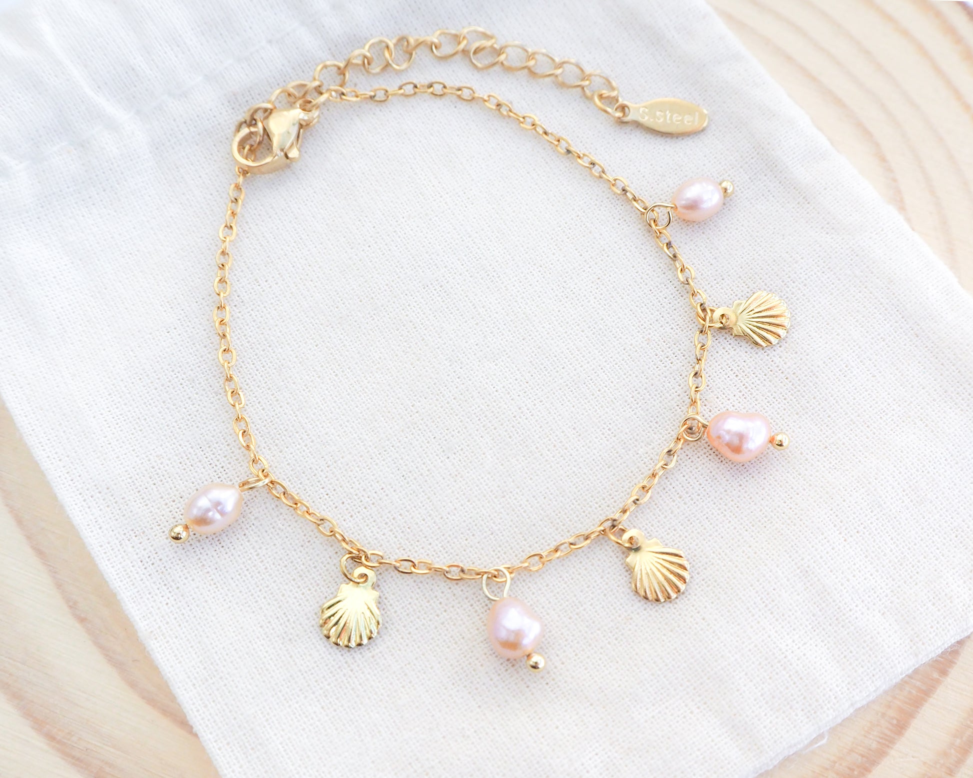 Gold bracelet with shell and pearl charms on a white surface. Gold Tiny Shell Rose Pink Freshwater Pearl Bracelet on display, Dainty Gold Shell Bracelet