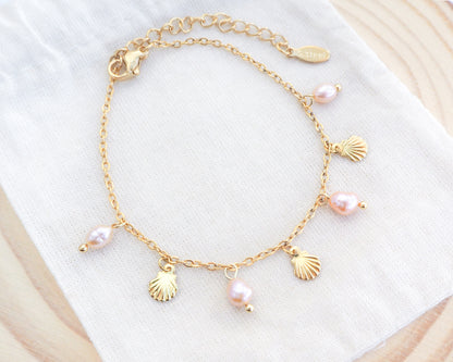 Gold bracelet with shell and pearl charms on a white surface. Gold Tiny Shell Rose Pink Freshwater Pearl Bracelet on display, Dainty Gold Shell Bracelet