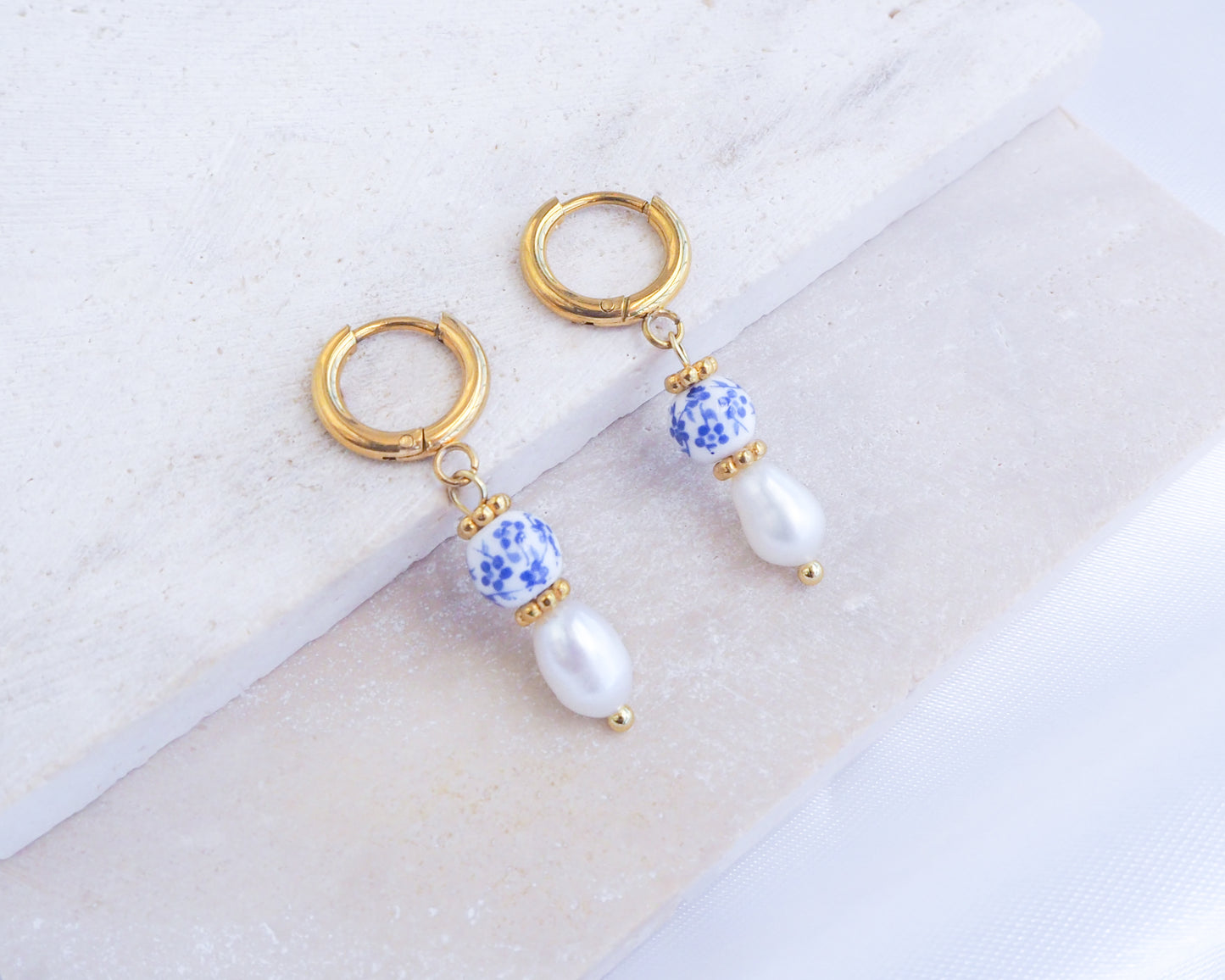 Pair of gold hoop earrings with blue and white bead accents on a light background. Portuguese Ceramic Pearl Mini Earrings on display, Mini Azulejo Earrings from Portugal, Portuguese Tlle Jewelry, Blue White Flower Porcelain Earrings