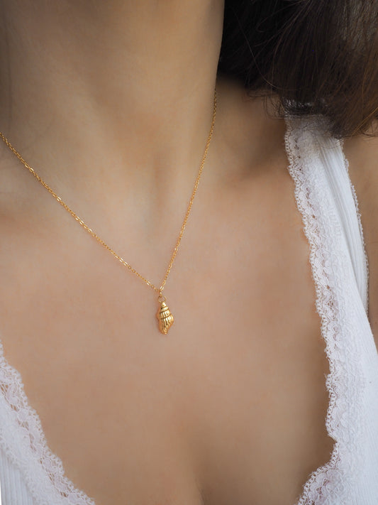 Gold necklace with a conch shell pendant worn by a model
