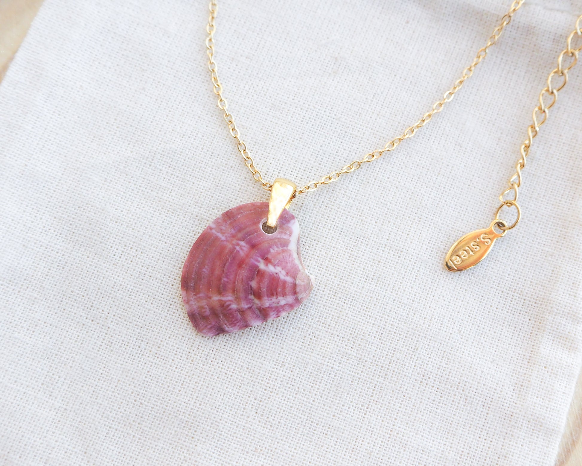 Side view of Bordeaux Fuchsia Venus Shell Gold Necklace on stone displayed