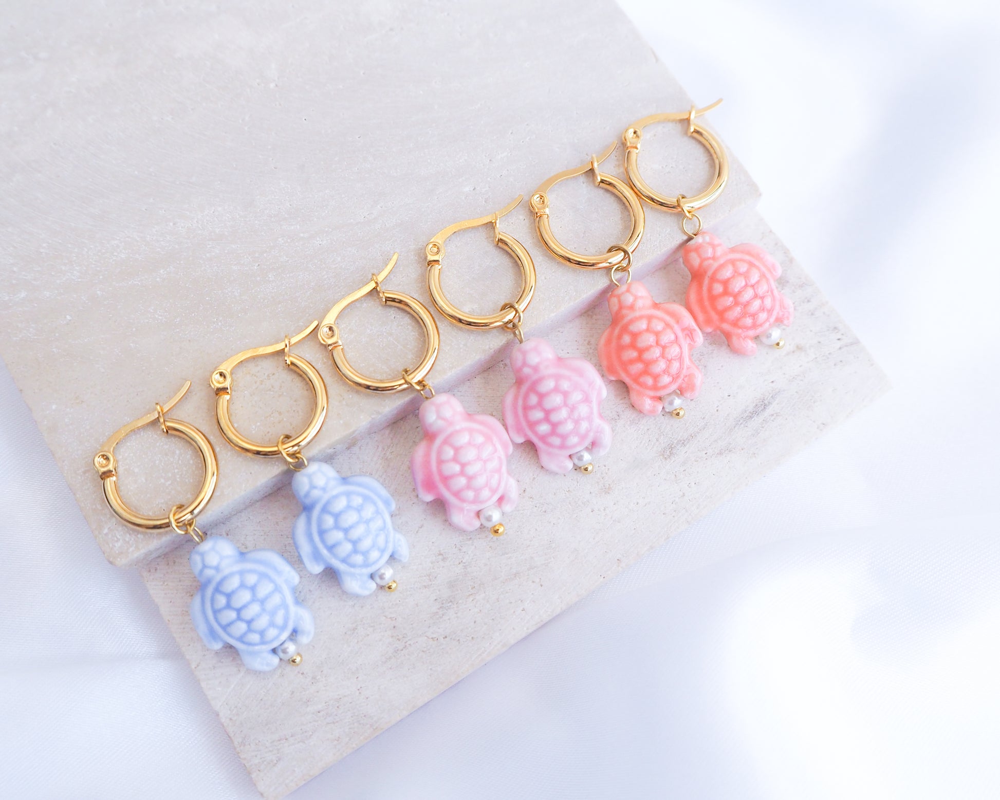 Set of colorful turtle-shaped earrings on a white background. Blue, Pink, Coral Turtle Ceramic Gold Earrings on display