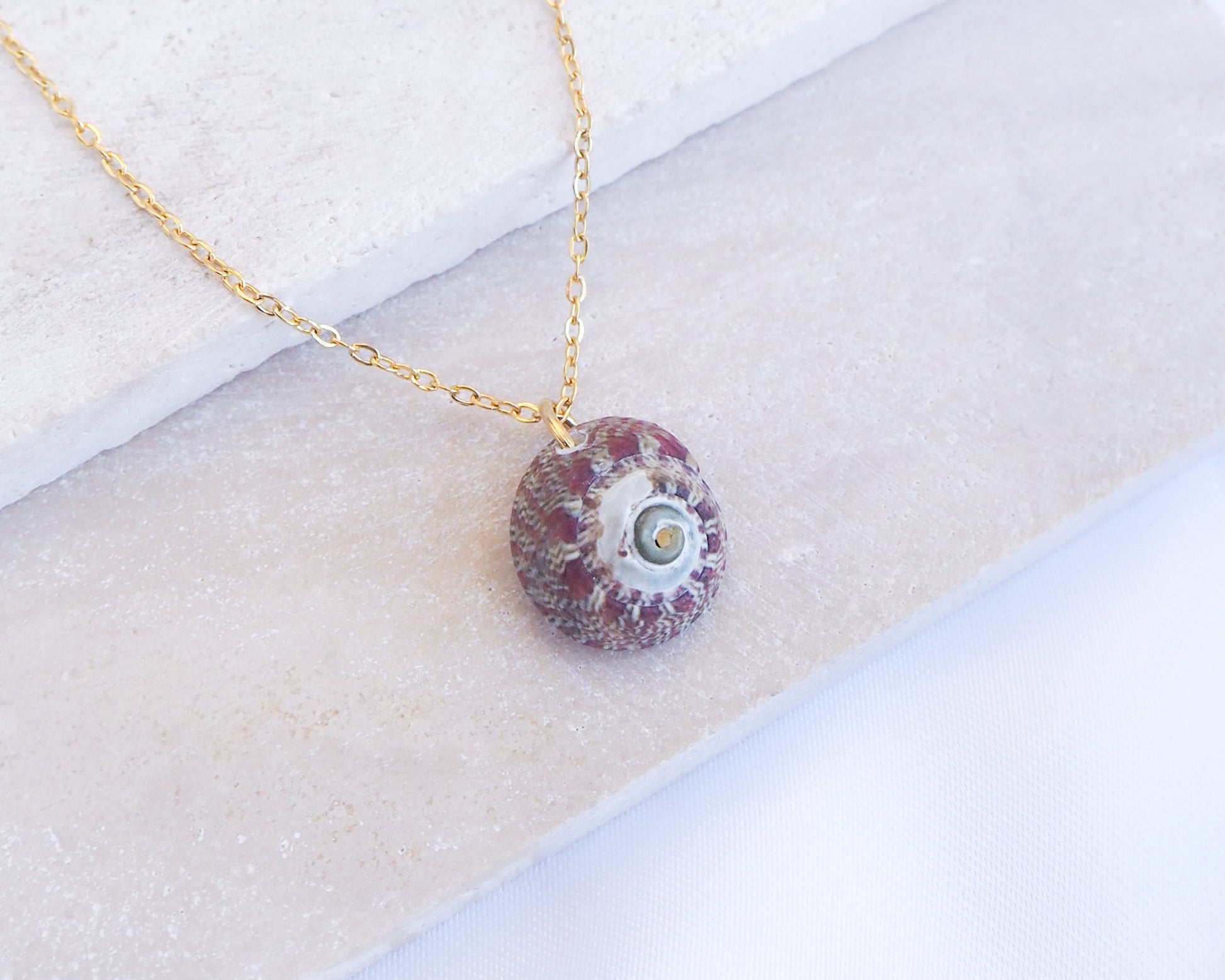Necklace with a red and white stone pendant on a textured surface. Bordeaux Green Patterned Flat Top Shell Gold Necklace on display close up
