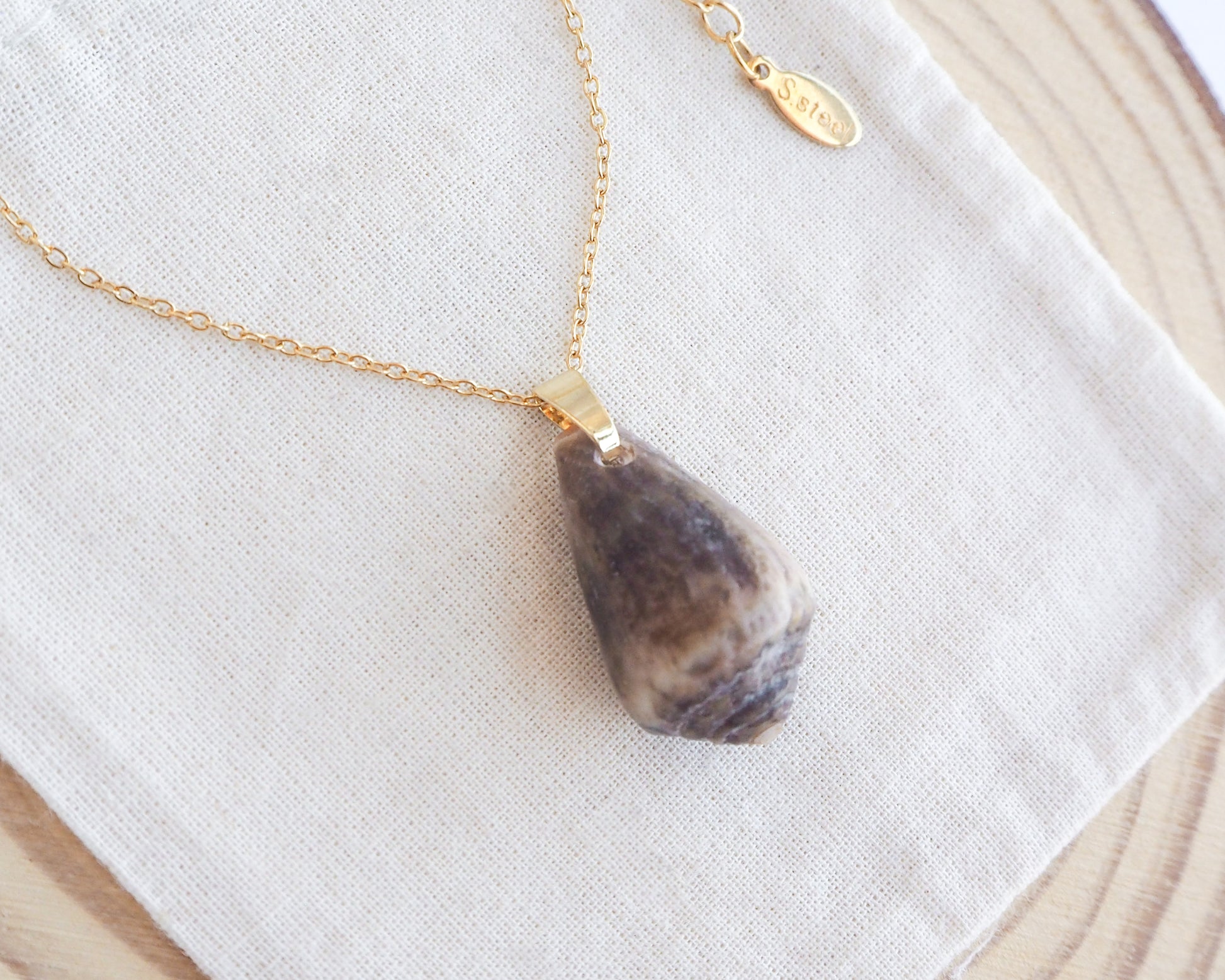 Necklace with a teardrop-shaped pendant on a white cloth background. Dark Mediterranean Cone Shell II Gold Necklace on display