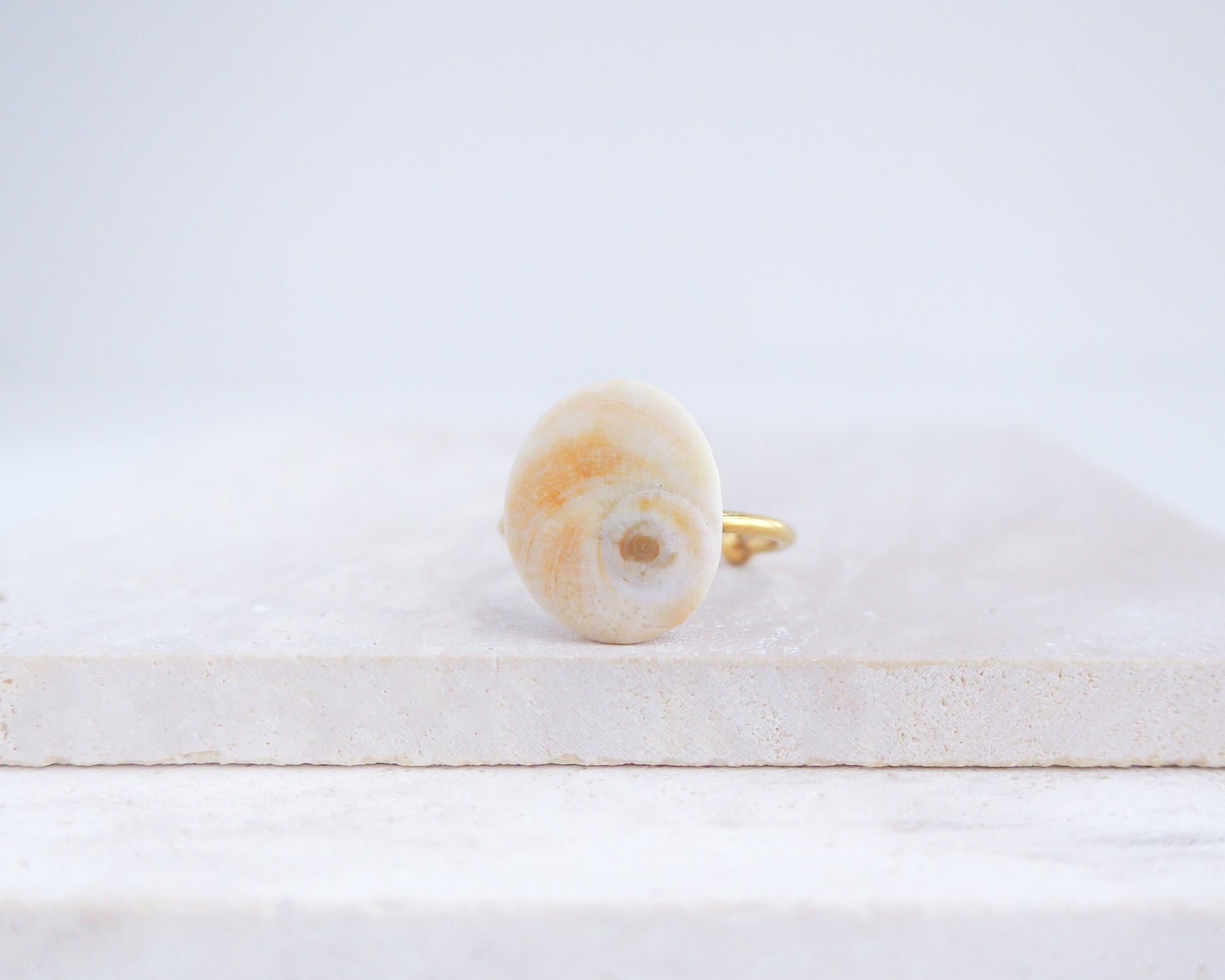 Soft yellow shiva eye ring on a white surface. Orange Yellow Eye of Saint Lucia Shell Gold Ring displayed on stone close up, Handcrafted Orange Shiva Eye Ring, Real Shiva Eye from Portugal, Handpicked eye of saint lucia, gold stainless steel ring