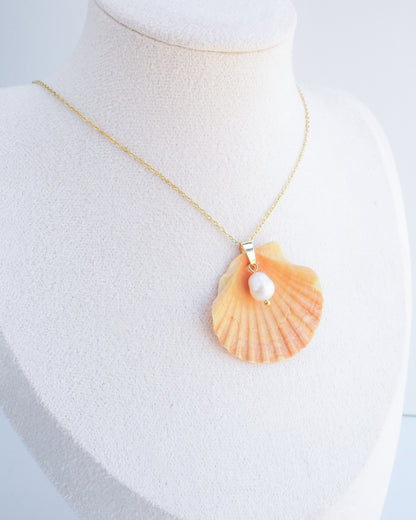 Necklace with a shell pendant and pearl on a mannequin bust. Display wearing Coral Orange Scallop Shell Pearl Gold Necklace II on stone displayed, Pilgrims Scallop Shell from Portugal with freshwater pearl and gold chain. 