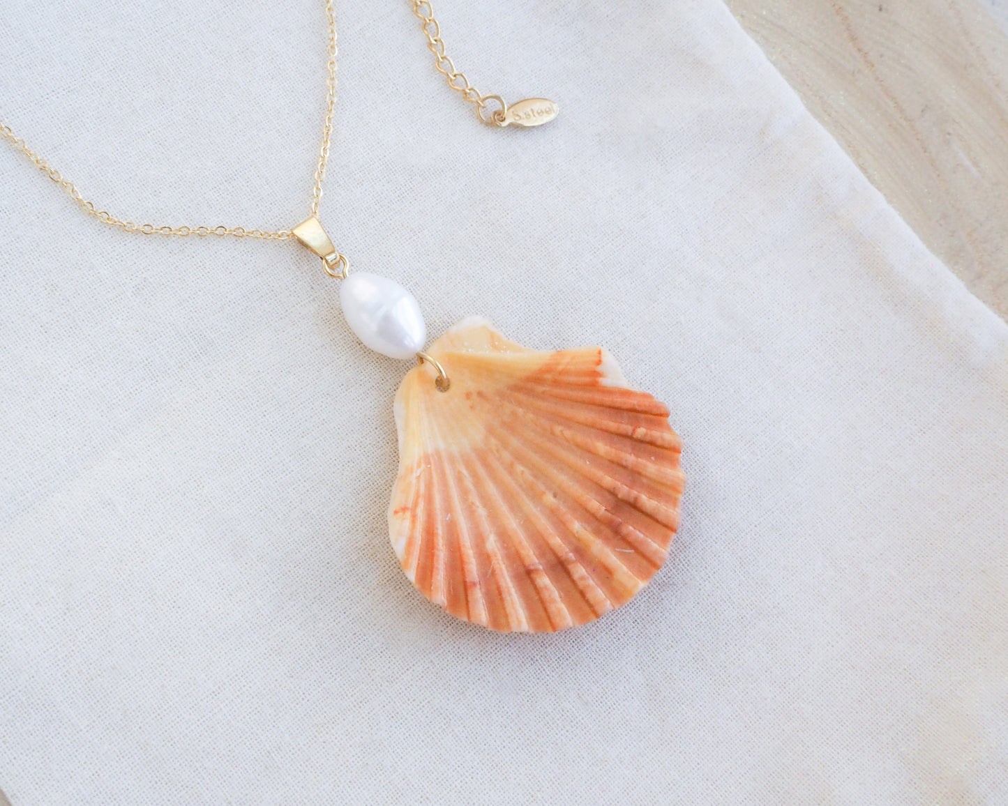 Necklace with a shell and pearl pendant on a light background. Coral Orange Scallop Shell Pearl Gold Necklace IV on display, Pilgrims Scallop Shell from Portugal with freshwater pearl and gold chain. 