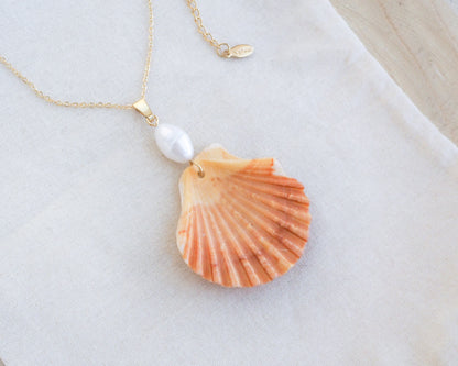 Necklace with a shell and pearl pendant on a light background. Coral Orange Scallop Shell Pearl Gold Necklace IV on display, Pilgrims Scallop Shell from Portugal with freshwater pearl and gold chain. 