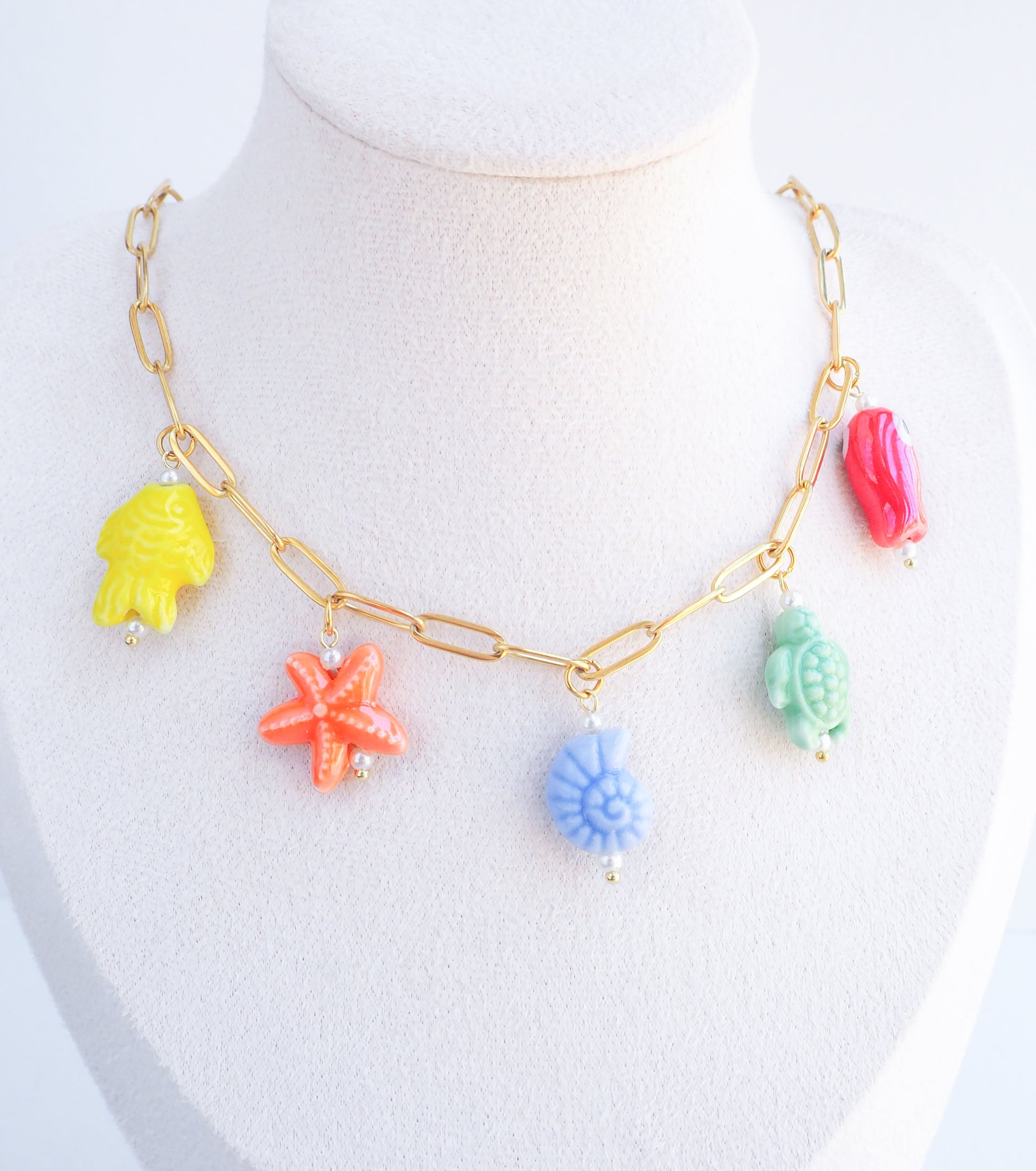 Displayed Rainbow Ceramic Charm Necklace with 5 ceramic ocean charms (turtle, starfish, fish, shell & more), sea treasure pendants, 18k gold stainless steel chain  