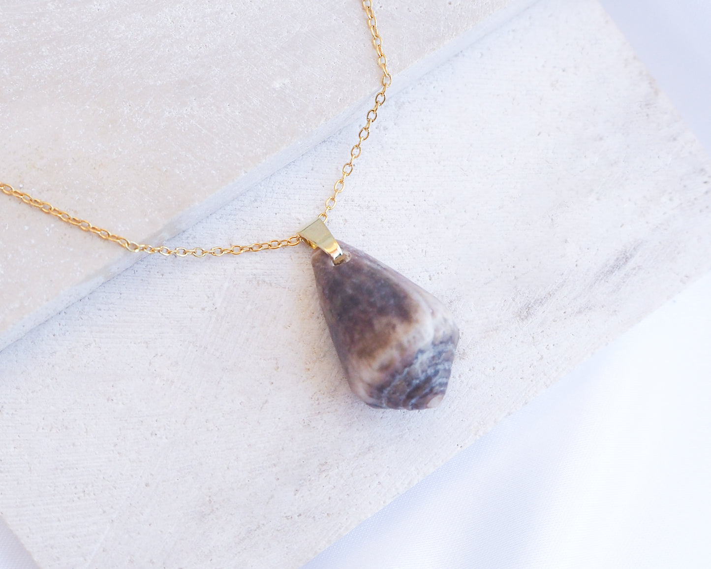 Dark Mediterranean Cone Shell II Gold Necklace displayed on stone 