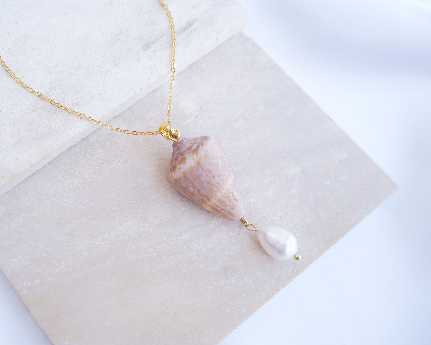 Close up of Model wearing Mediterranean Cone Shell Pearl Necklace Reversed from Portugal on stone, handpicked cone shell from Algarve, Freshwater pearl and 18k gold stainless steel chain