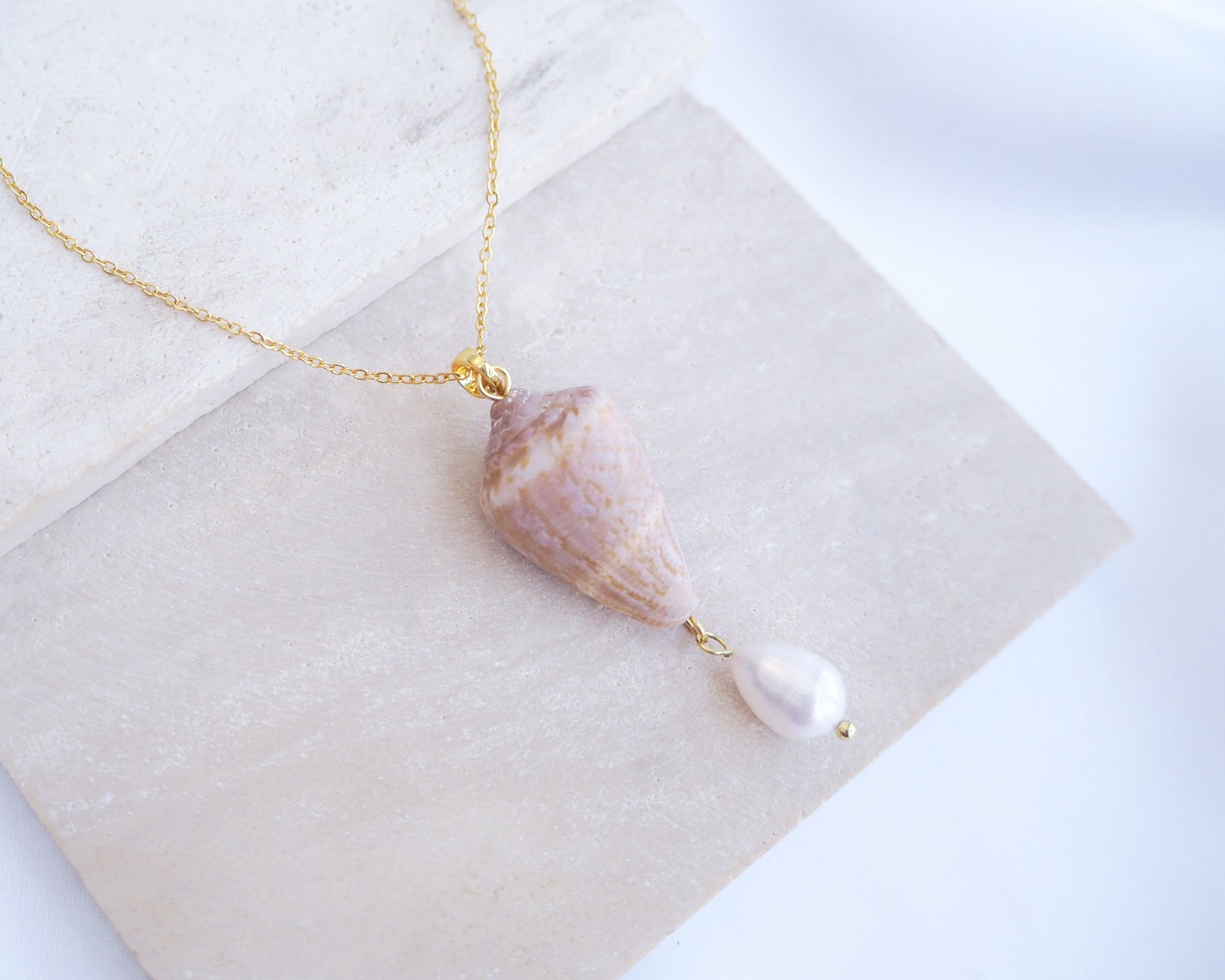 Close up of Model wearing Mediterranean Cone Shell Pearl Necklace Reversed from Portugal on stone, handpicked cone shell from Algarve, Freshwater pearl and 18k gold stainless steel chain