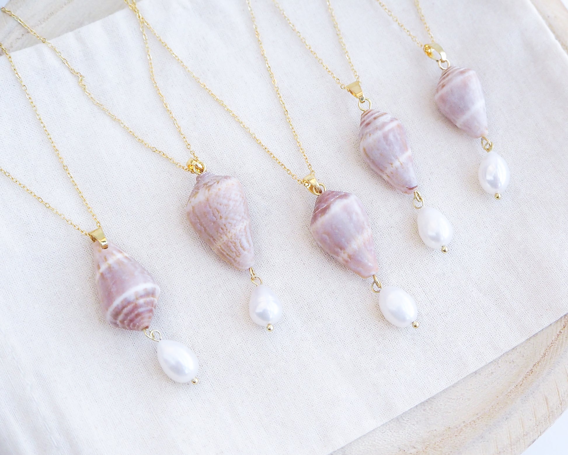 Necklaces with shell and pearl pendants on a white surface. Mix of Mediterranean Cone Shell Pearl Necklaces from Portugal on display, handpicked cone shell from Algarve, Freshwater pearl and 18k gold stainless steel chain