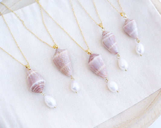 Necklaces with shell and pearl pendants on a white surface. Mix of Mediterranean Cone Shell Pearl Necklaces from Portugal on display, handpicked cone shell from Algarve, Freshwater pearl and 18k gold stainless steel chain