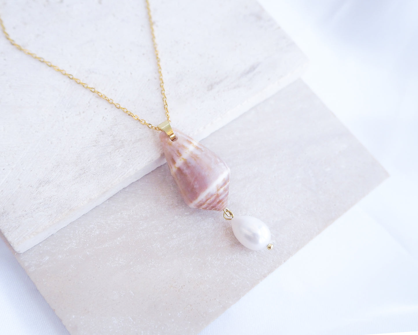 Necklace with shell and pearl pendant on a white fabric background. Mediterranean Cone Shell Pearl Necklace Reversed II