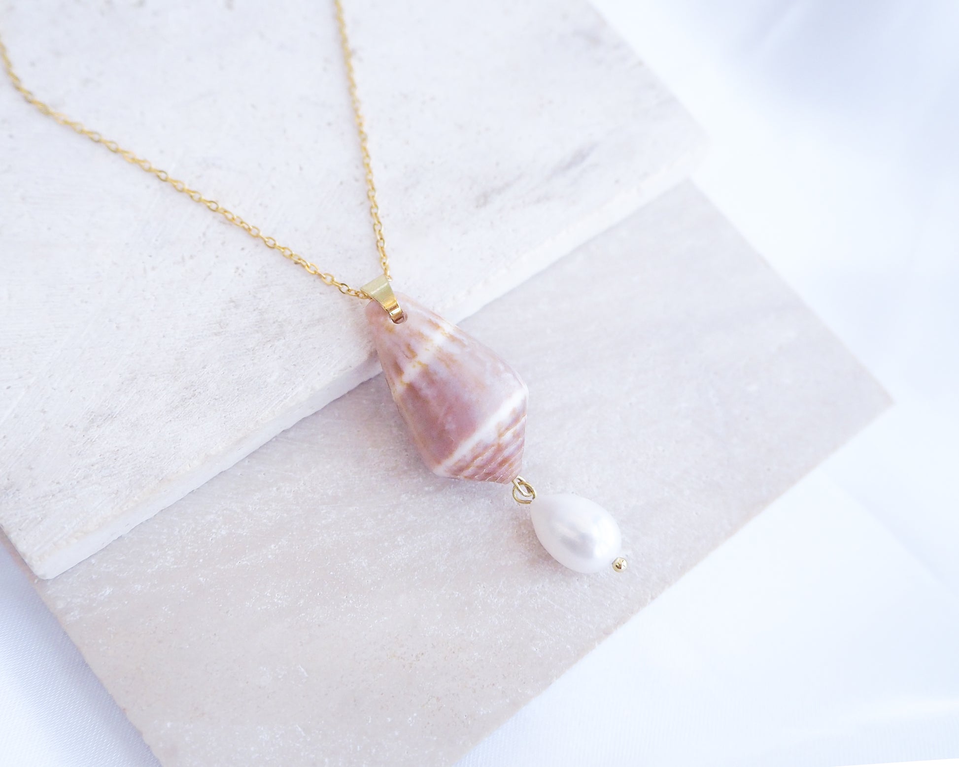 Necklace with shell and pearl pendant on a white fabric background. Mediterranean Cone Shell Pearl Necklace Reversed II