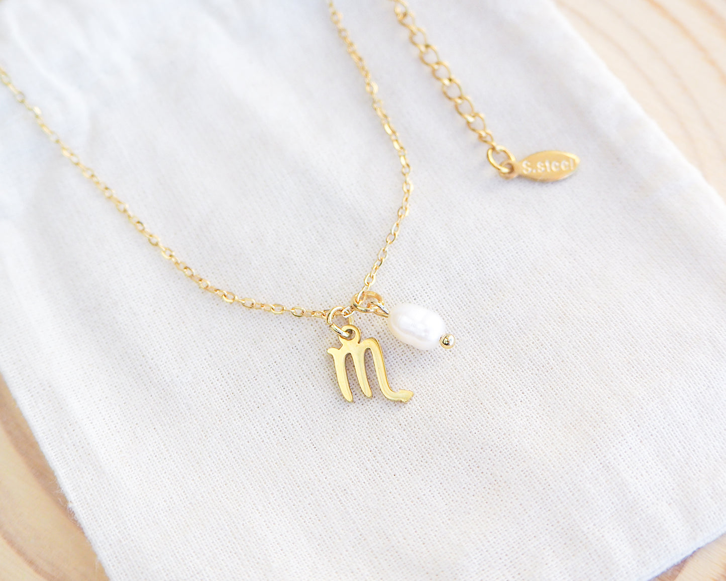 Close up of Gold Scorpio Zodiac Pearl Necklace on display, made with 18k gold stainless steel and white freshwater pearl 