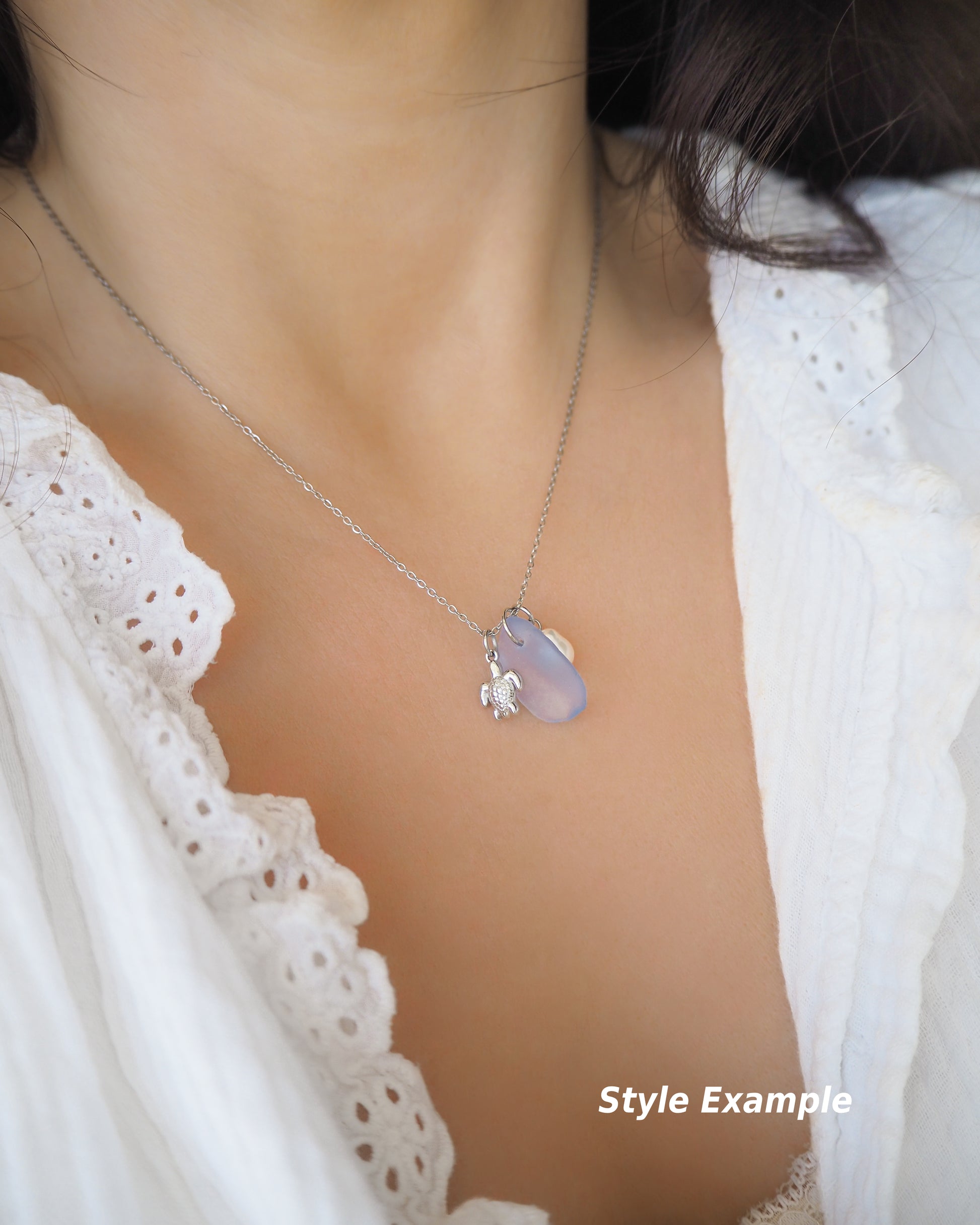 Model wearing a silver necklace with a tiny turtle pendant, light blue sea glass and freshwater pearl pendant on neck with white shirt. Made with silver stainless steel chain. This photo is a style example for reference how this necklace will fit.