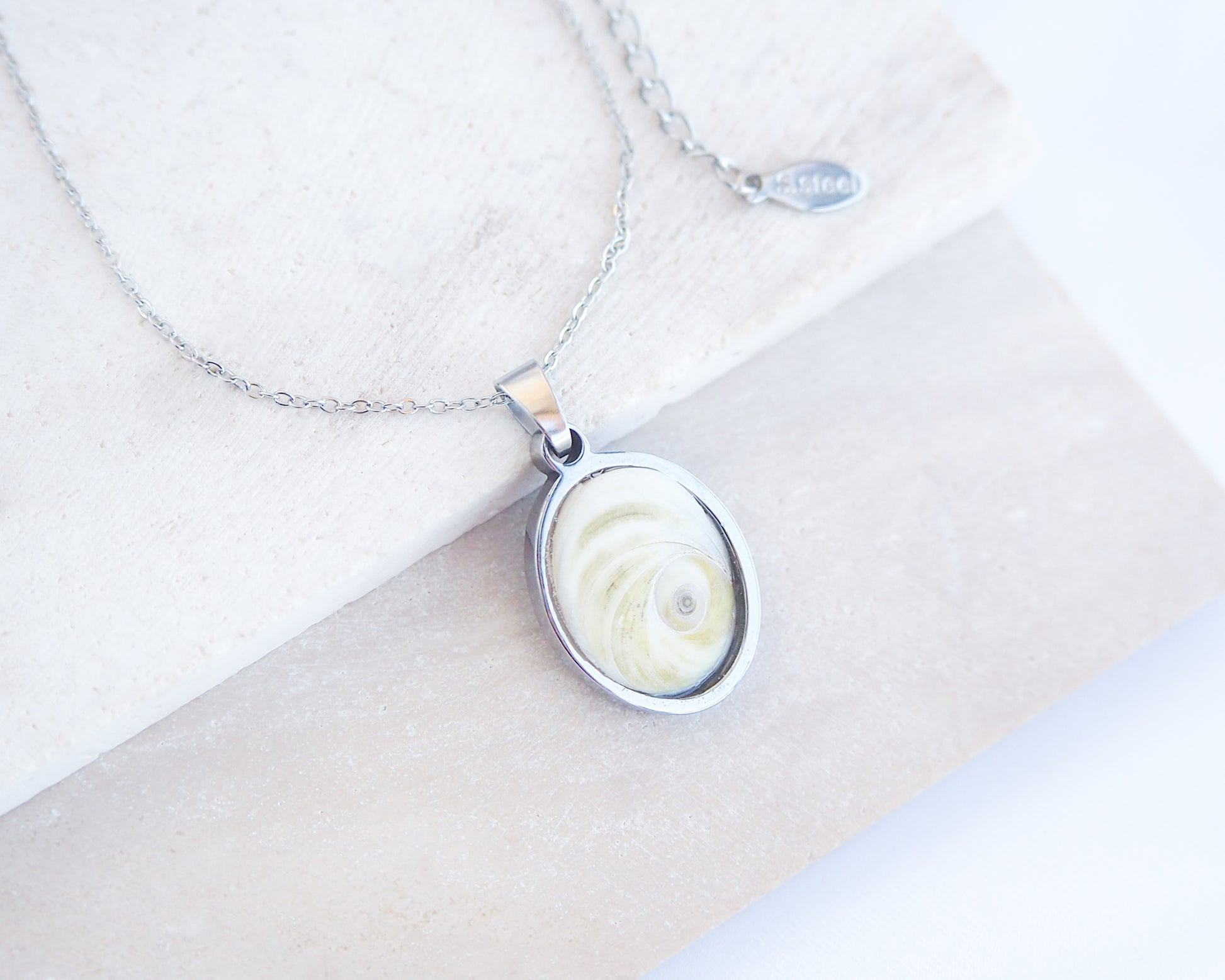 Eye of Saint Lucia Silver Necklace front view with plant background, silver stainless steel shiva eye pendant necklace, Saint Lucy Eye, operculum pendant