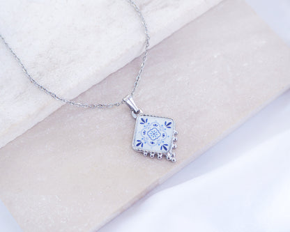 Close up of Portuguese Tile Necklace Blue Blossom Silver on stone displayed. Made with silver stainless steel and white blue floral pendant inspired by the Portuguese Azulejo design pattern. 