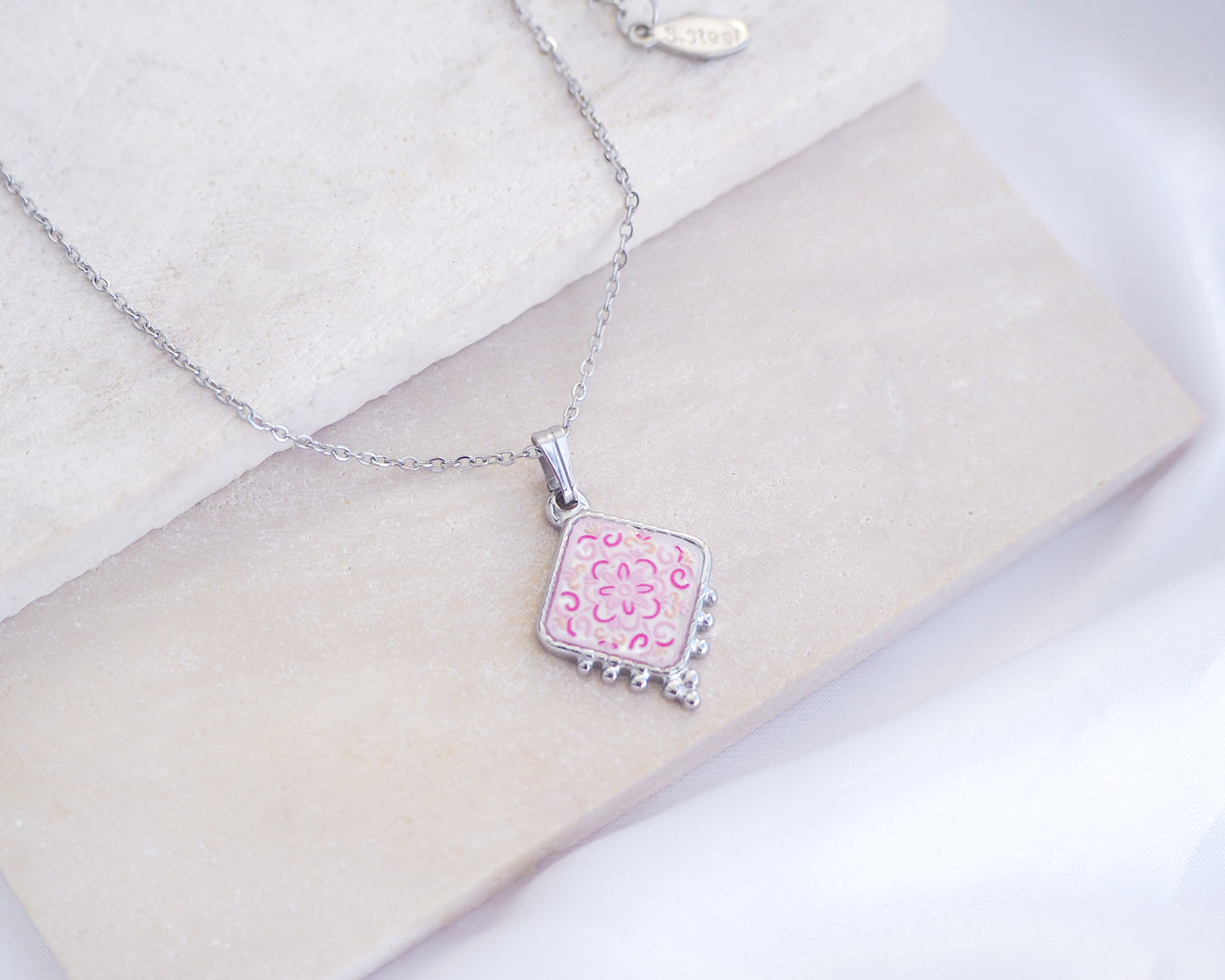 Close up of Portuguese Tile Necklace Floral Pink silver on stone displayed. Made with silver stainless steel and white pink floral pendant inspired by the Portuguese Azulejo design pattern. 