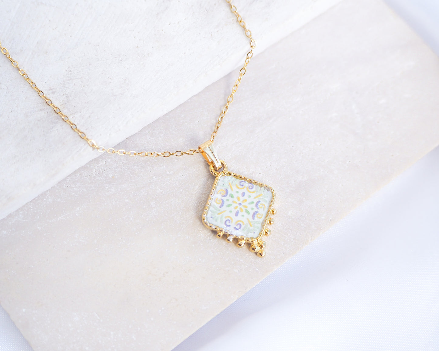 Close up of Soft Yellow Green Portuguese Tile Necklace Gold on stone displayed. Made with 18k gold stainless steel and soft floral pendant inspired by the Portuguese Azulejo design pattern. 