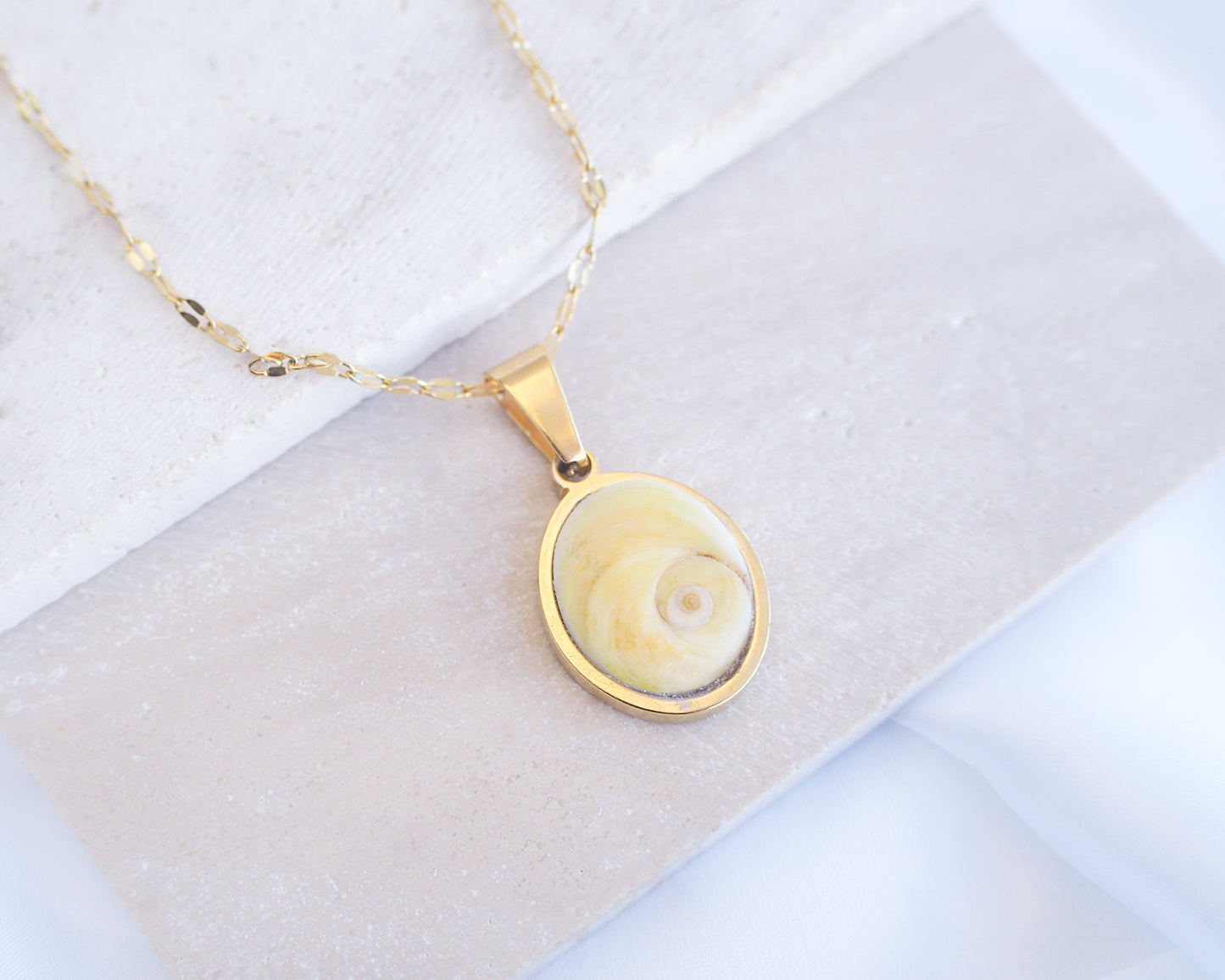Soft Yellow Shiva Eye Deluxe Necklace II on stone displayed. Light Eye of Saint handpicked from Portugal, 18k gold stainless steel shiva eye pendant necklace, Saint Lucy Eye, operculum pendant