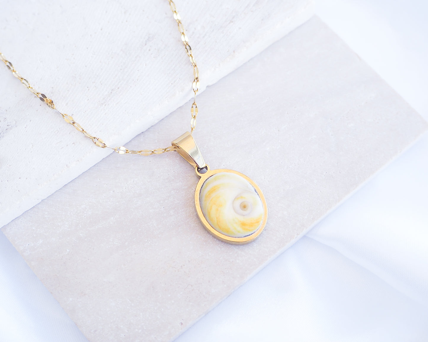 Soft Yellow Shiva Eye Necklace on stone displayed. Light Eye of Saint handpicked from Portugal, 18k gold stainless steel shiva eye pendant necklace, Saint Lucy Eye, operculum pendant