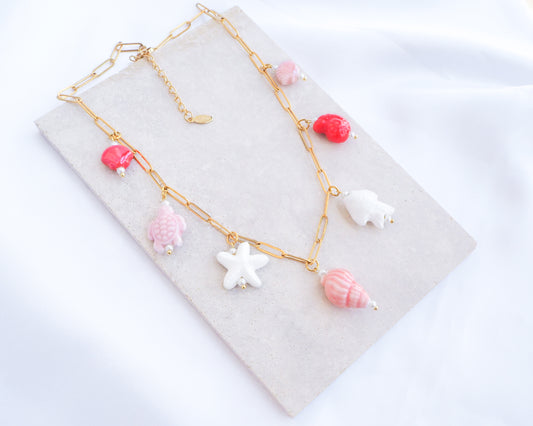 Sweet Ocean Ceramic Charm Necklace with 7 ceramic ocean charms (turtle, starfish, fish, shell & more), Pink white red sea pendants, 18k gold stainless steel chain displayed on stone 