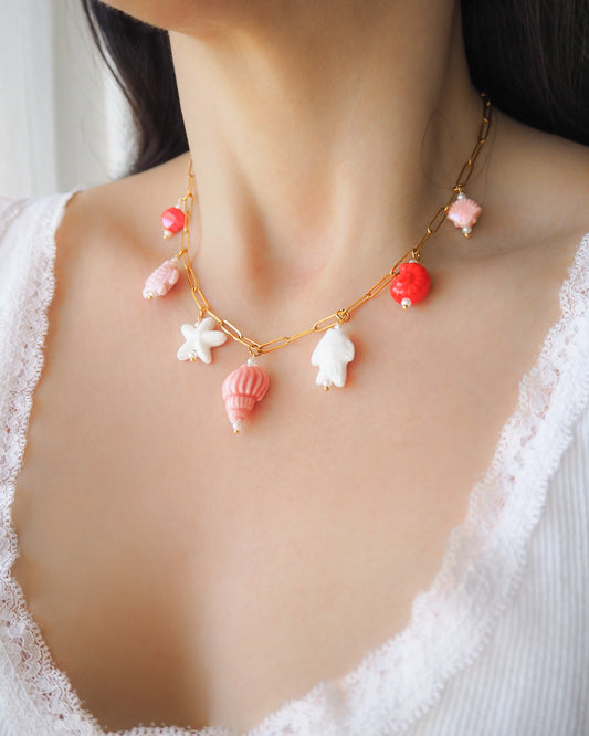 Model wearing Sweet Ocean Ceramic Charm Necklace with 7 ceramic ocean charms (turtle, starfish, fish, shell & more), Pink white red sea pendants, 18k gold stainless steel chain  