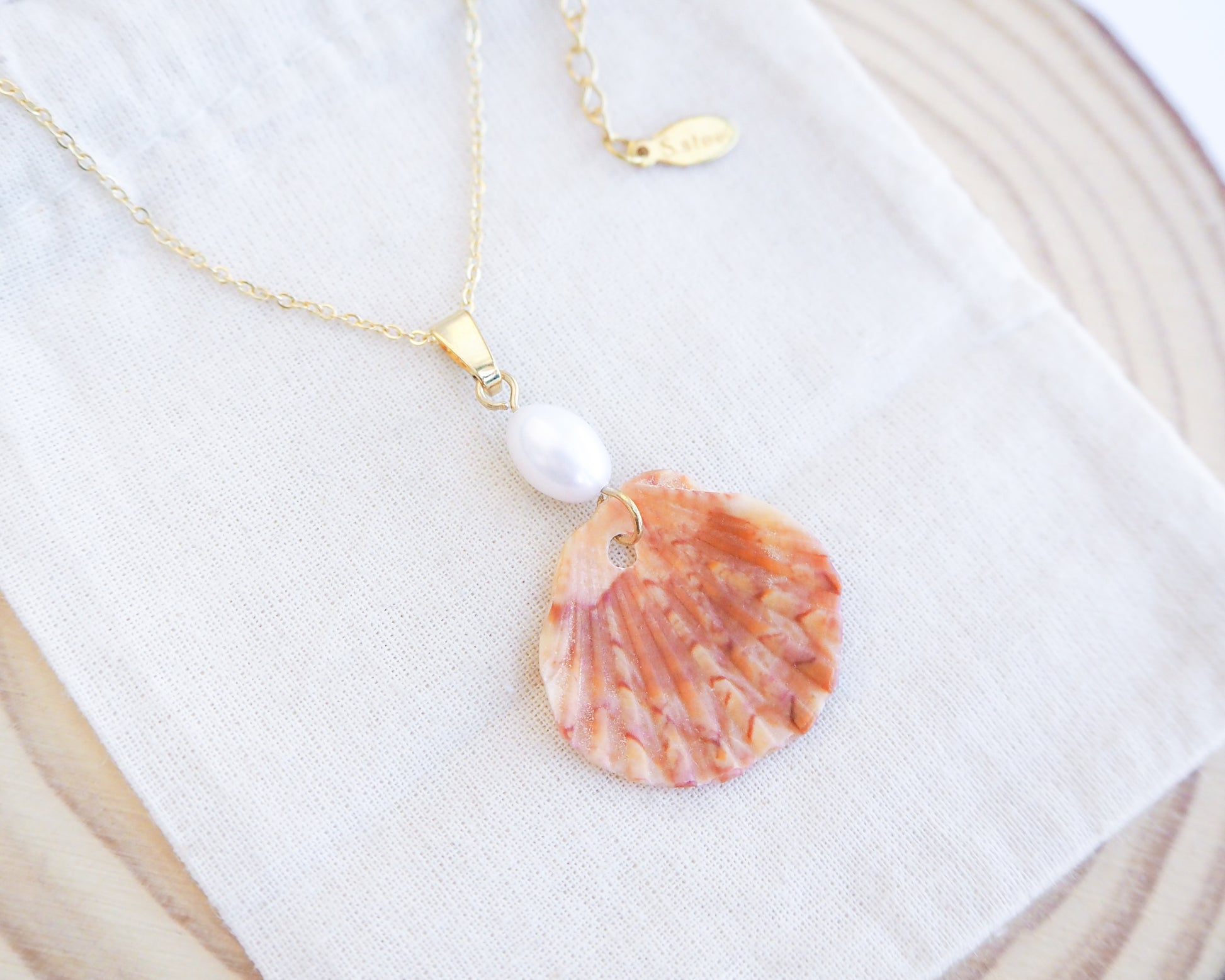 Close up of Tiny Coral Scallop Shell Pearl Necklace on cotton displayed