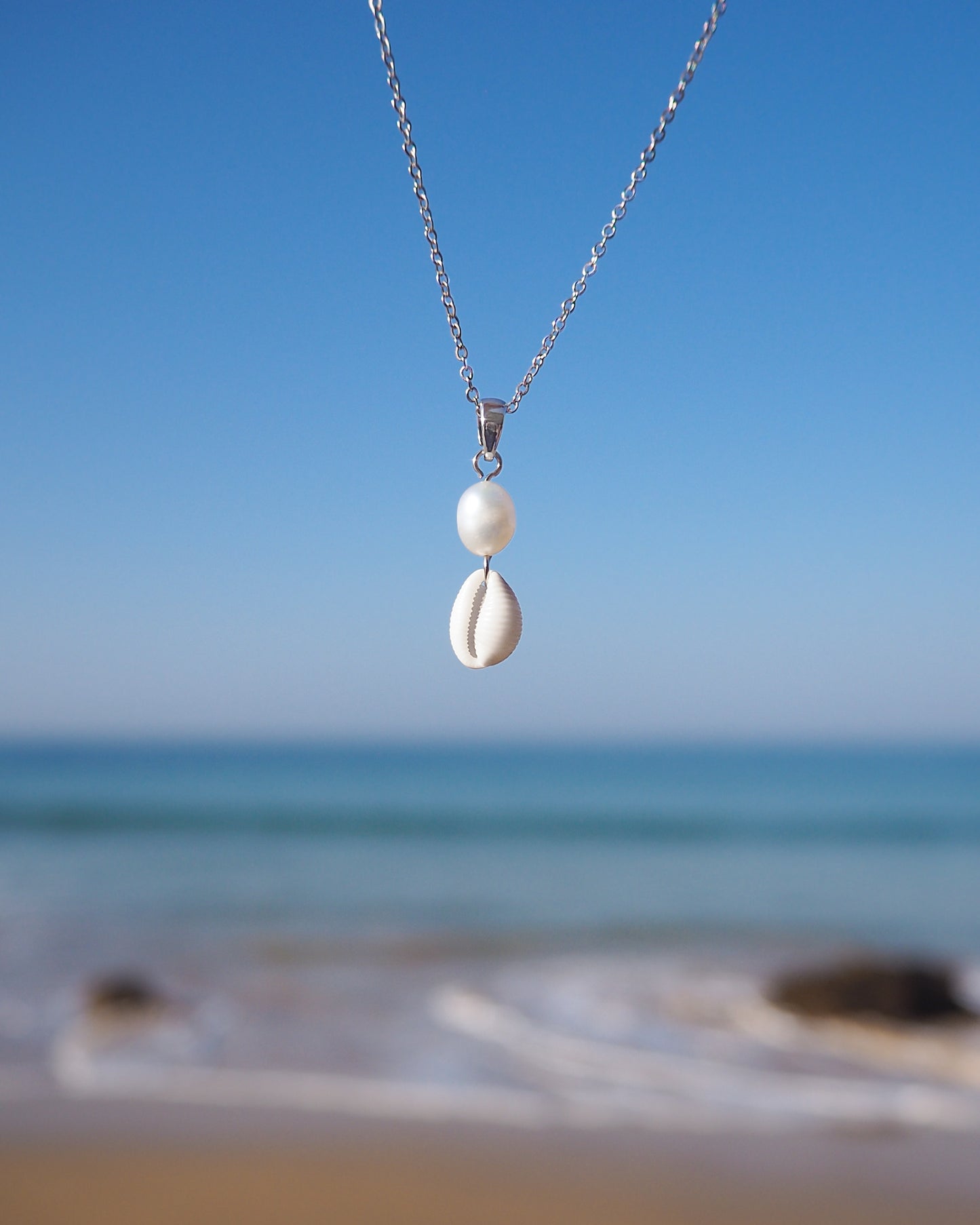 Tiny Cowrie Shell Pearl Necklace Silver with ocean background. Real Cowrie Shell from Portugal, Freshwater Pearls and silver stainless steel chain.