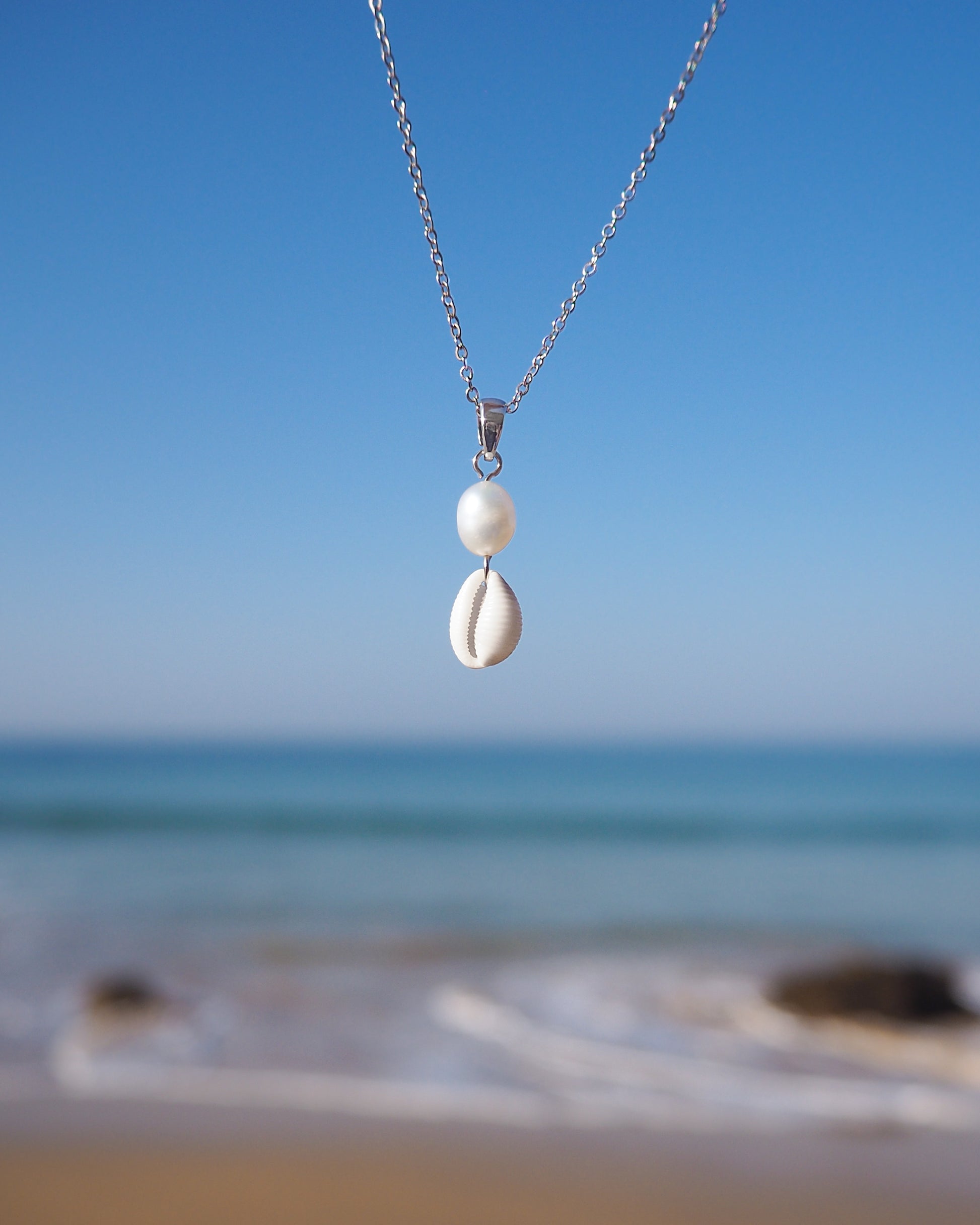 Tiny Cowrie Shell Pearl Necklace Silver with ocean background. Real Cowrie Shell from Portugal, Freshwater Pearls and silver stainless steel chain.