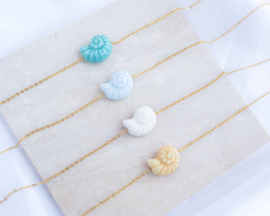 Tropical Ocean Blue Ceramic Seashell Nautilus Gold Necklaces displayed on stone