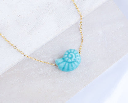 Turquoise Blue Ceramic Seashell Nautilus Gold Necklace on stone display 