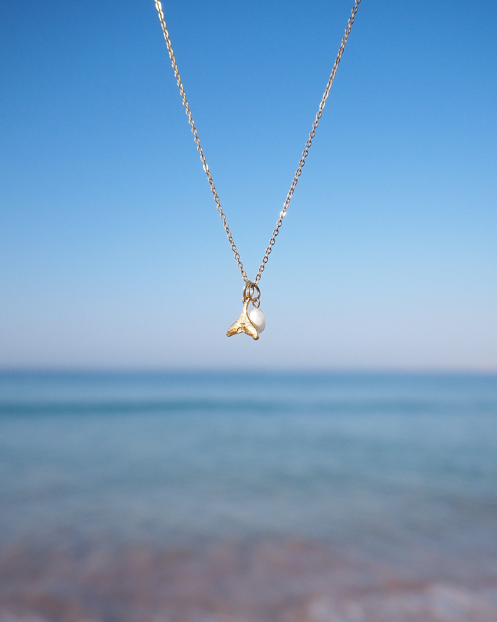 Gold Whale Tail Pearl Necklace with ocean background, 18k gold stainless steel and white freshwater pearl