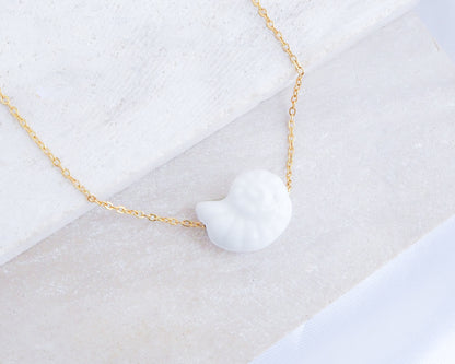 White Ceramic Seashell Nautilus Gold Necklace displayed on stone